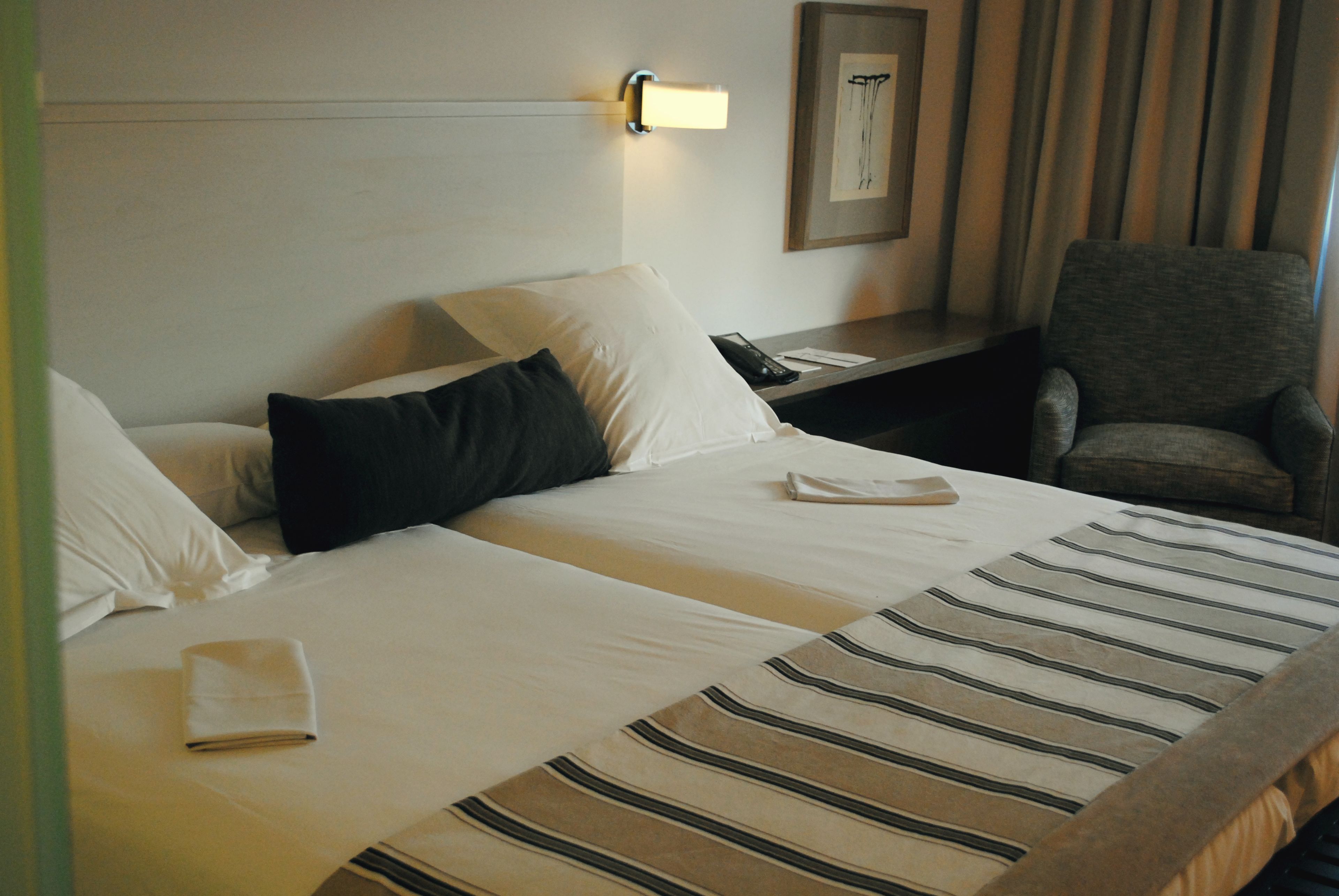 A hotel room with two beds, a nightstand, a chair, and a framed picture on the wall.