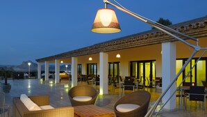 Een terras buiten met rieten meubilair, een houten tafel en een hanglamp.