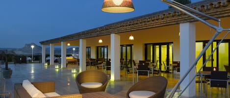 An outdoor patio area with wicker furniture, a wooden table, and a hanging lamp.