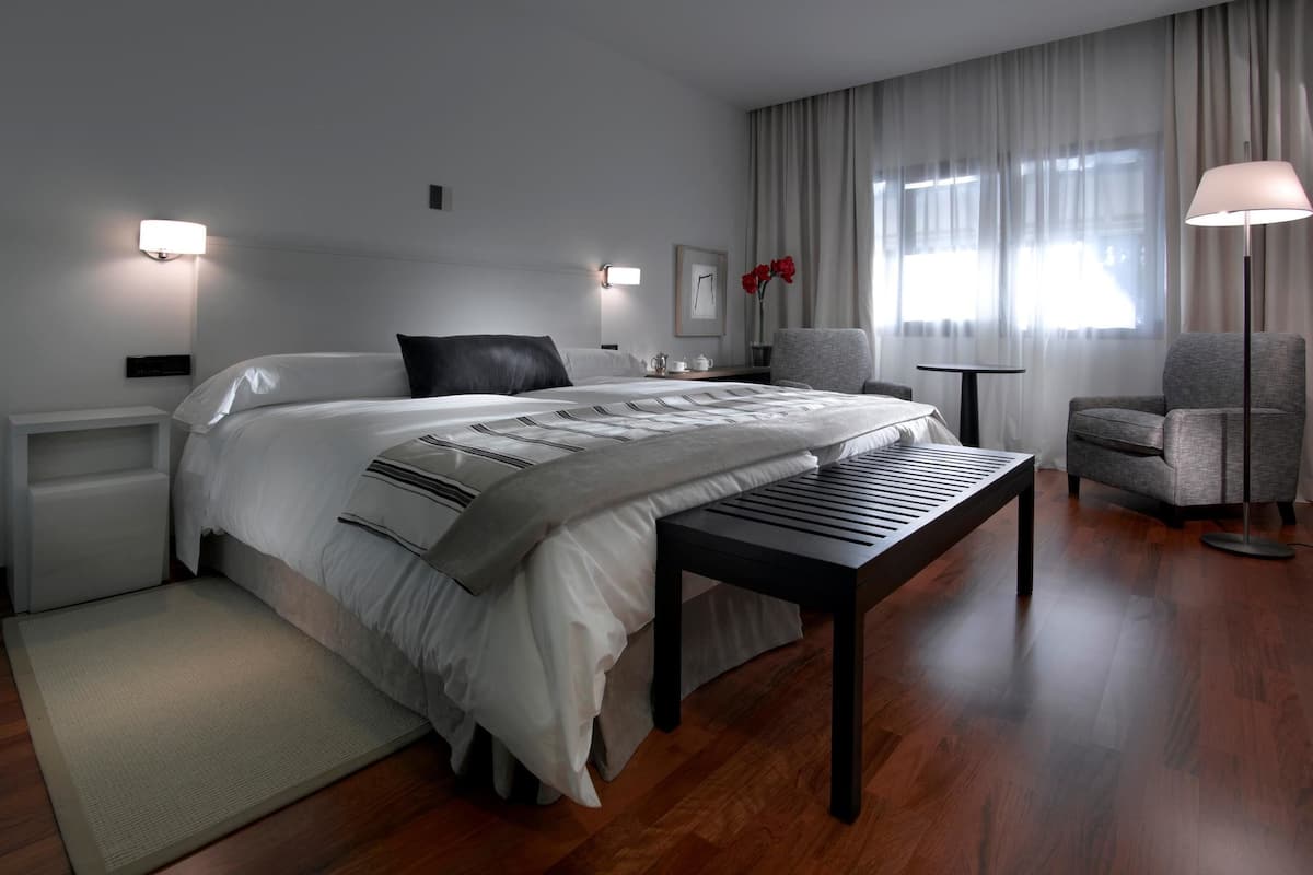 Une chambre d’hôtel moderne avec un grand lit, une table de chevet, une chaise, une petite table et une lampe.