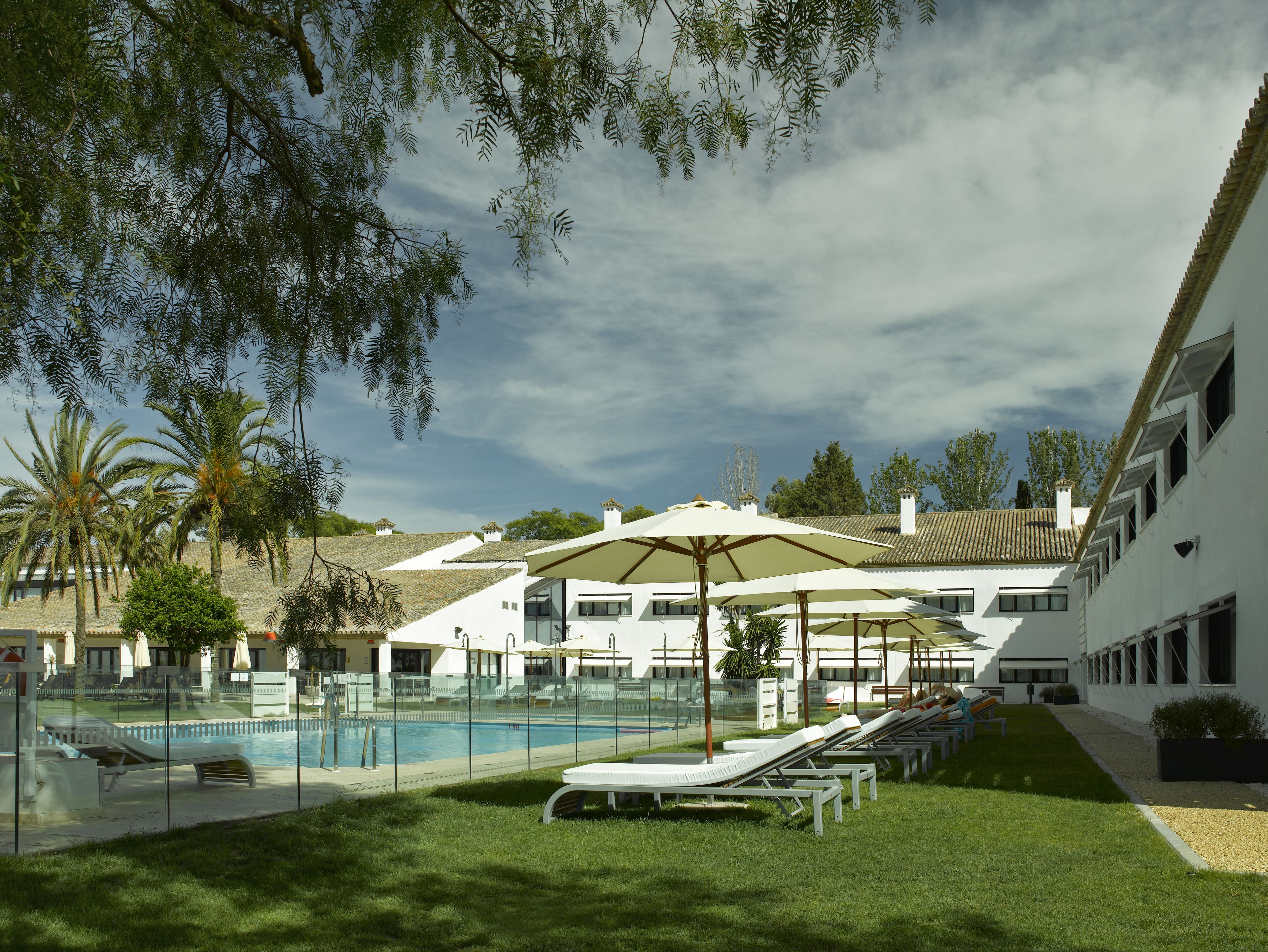 A poolside area with lounge chairs and umbrellas, a swimming pool, and a building with a tiled roof.