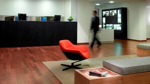 Een moderne kantoorruimte met een receptiebalie, een rode bureaustoel, een houten salontafel en een televisie.