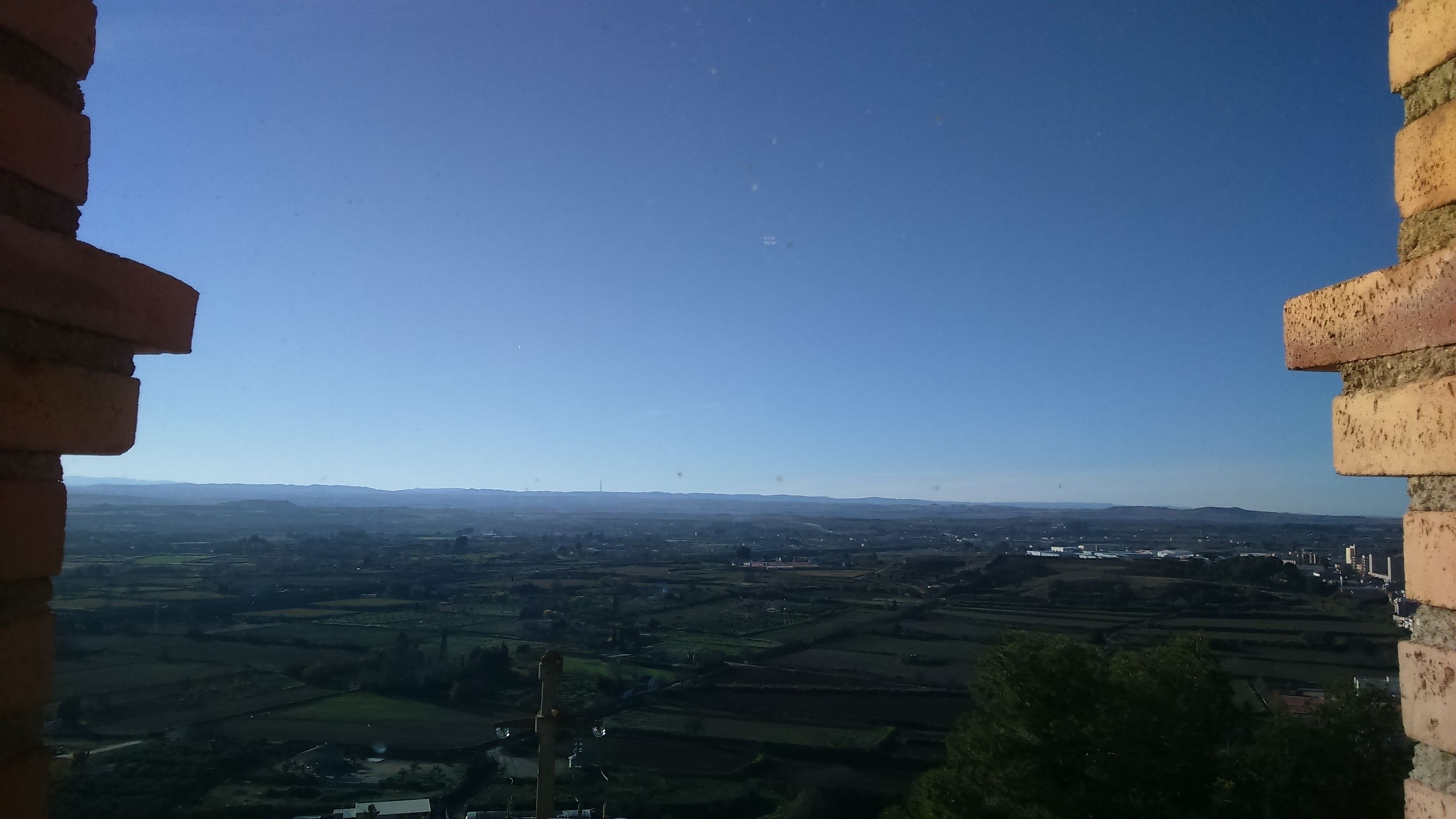 A view from a window overlooking a rural landscape with fields and distant buildings.