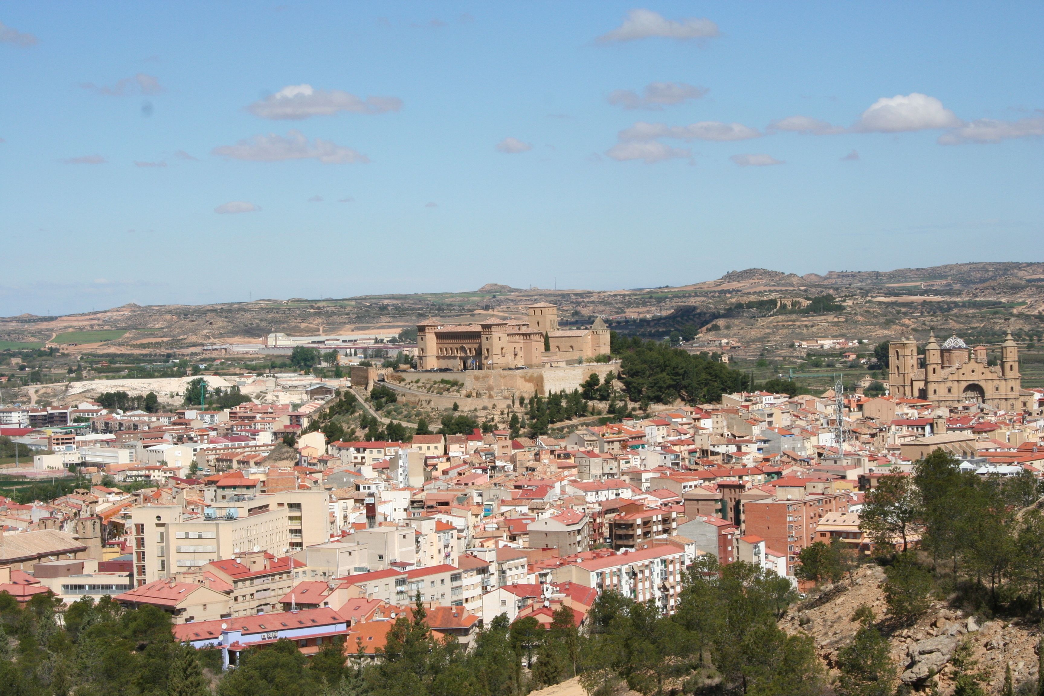 A cityscape with a prominent historical fortress on a hill, surrounded by densely packed buildings with red-tiled roofs.