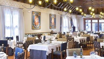 A dining area with multiple tables and chairs, ornate wall decorations, and a chandelier.