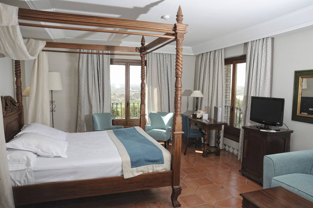 Ein Bett mit Baldachin, ein Schreibtisch mit Stuhl, ein Fernseher und Blick ins Freie.