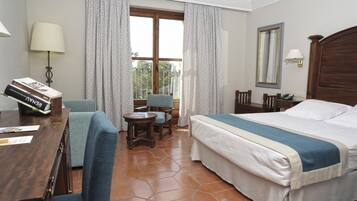 A hotel room with a bed, a desk with a lamp, a chair, a small table, and curtains.