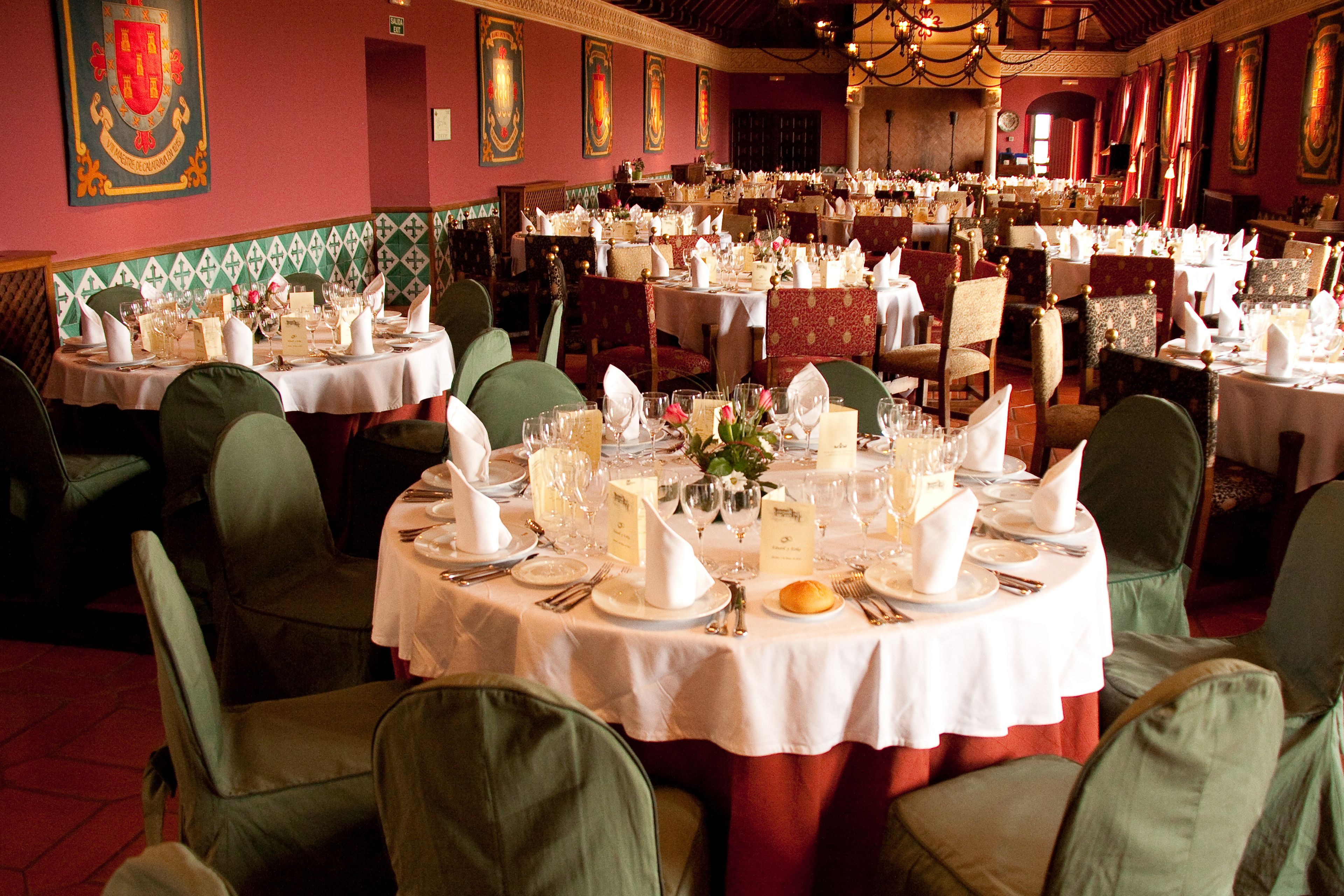 Un salón de banquetes con varias mesas redondas dispuestas para comer, cada una con sillas tapizadas en verde.