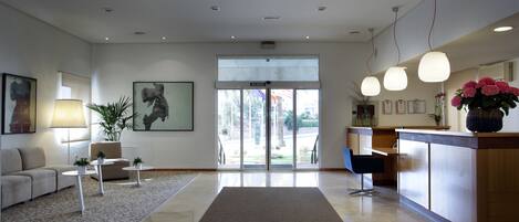 A modern hotel lobby with a reception desk, a sofa, a coffee table, and a large window.