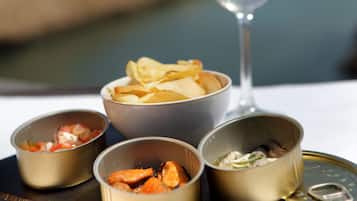 A table with four bowls of food and a glass of white wine, set against a backdrop of a body of water and distant buildings.