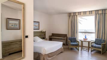 A hotel room with a bed, bedside table, lamp, chair, and a view of the sea through curtains.