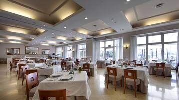 A spacious dining area with multiple tables and chairs, large windows, and a modern ceiling design.