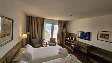 Habitación de hotel con dos camas, un escritorio, una silla, un televisor y un balcón con cortinas.