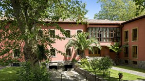 Un edificio rosa con varias ventanas y un patio con palmeras y un puente de madera.
