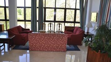 Una habitación amplia con ventanas grandes, un sofá rojo, un reposapiés estampado y una planta en maceta.