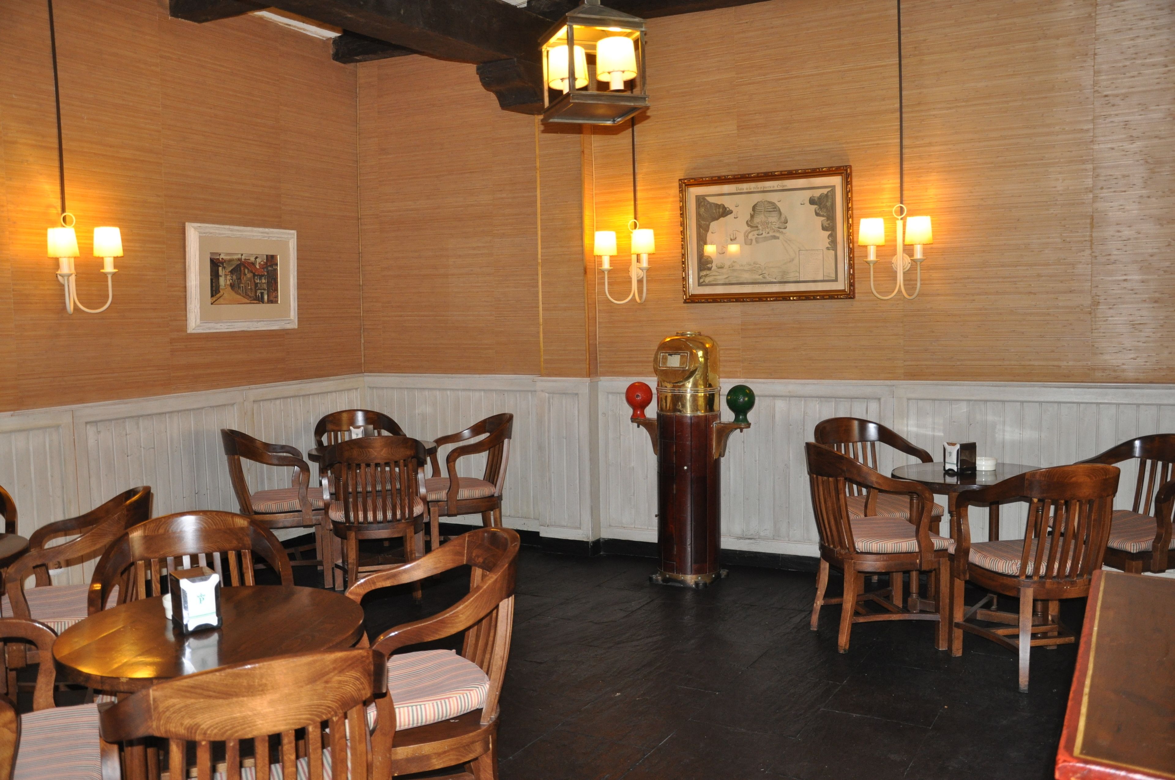 A dining area with wooden tables and chairs, wall-mounted light fixtures, and framed artwork.