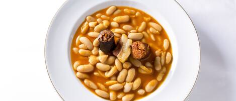 Un plato blanco con sopa de frijoles y trozos de salchicha.