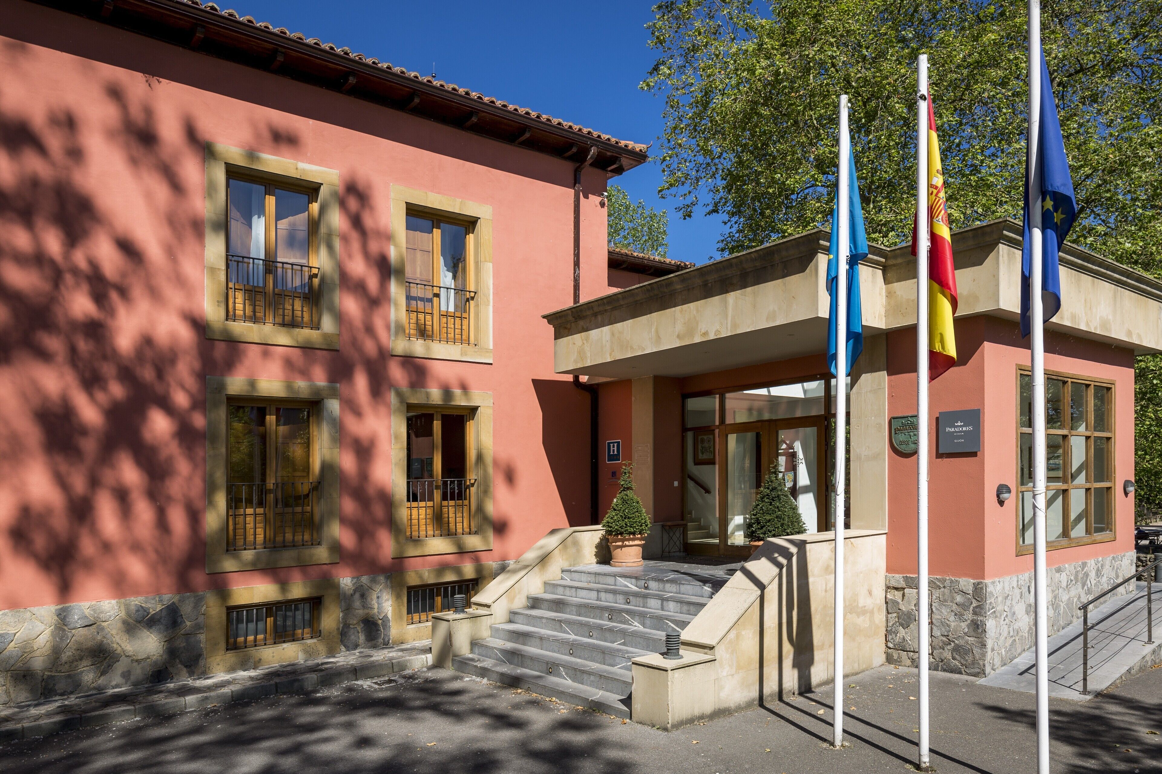 Ein Gebäude mit roter Fassade, zahlreichen Fenstern und einer Treppe, die zum Eingang führt.