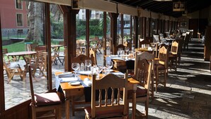 Un restaurante al aire libre con mesas y sillas de madera, amplias ventanas y suelo de piedra.