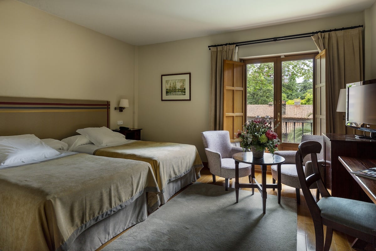 Una habitación de hotel con dos camas, un escritorio, una silla, un televisor y una ventana con cortinas.
