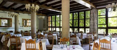 Un comedor con mesas y sillas de madera, ventanas amplias y candelabros.