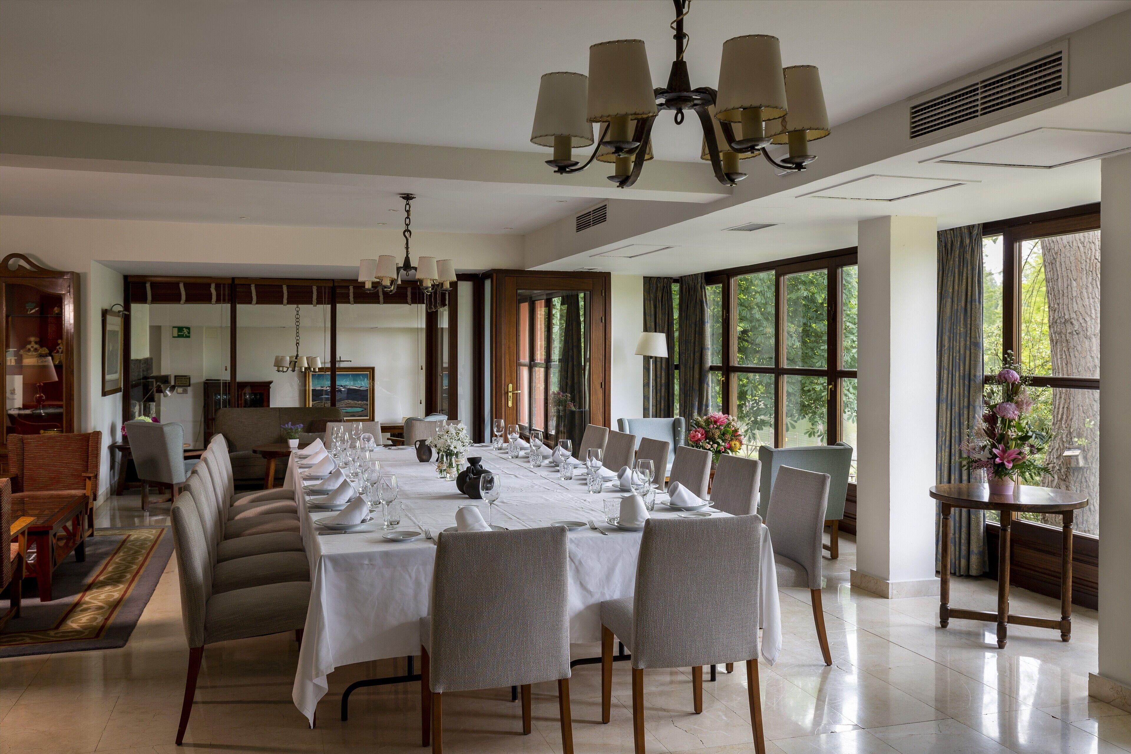 Uma sala de jantar com uma mesa comprida posta para refeição, cercada por cadeiras, e um lustre acima.