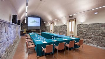 A conference room with long tables and chairs, a screen displaying 'Paradise', and stone walls.