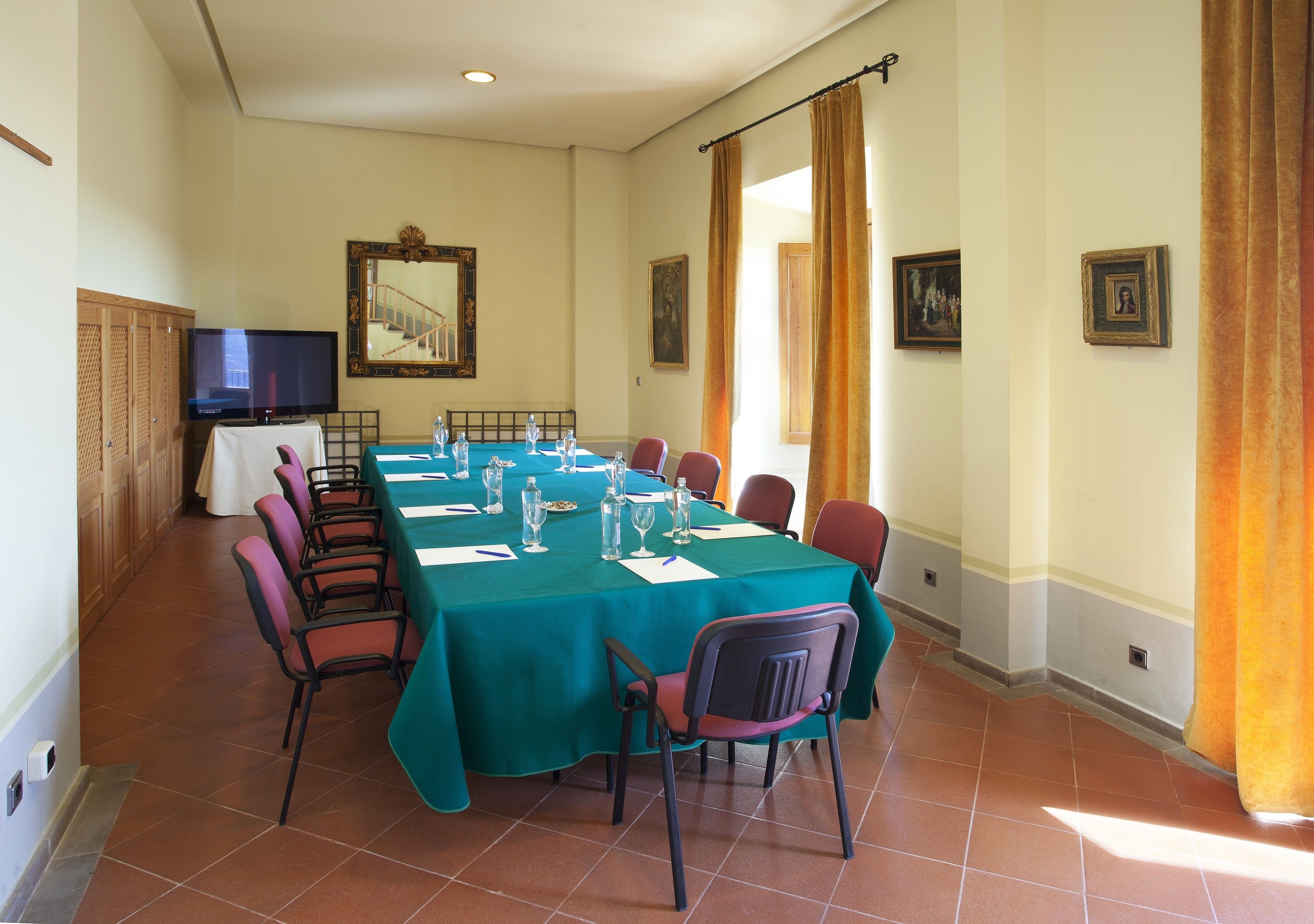 Un salón de conferencias con una larga mesa, sillas, un televisor y cuadros en las paredes.