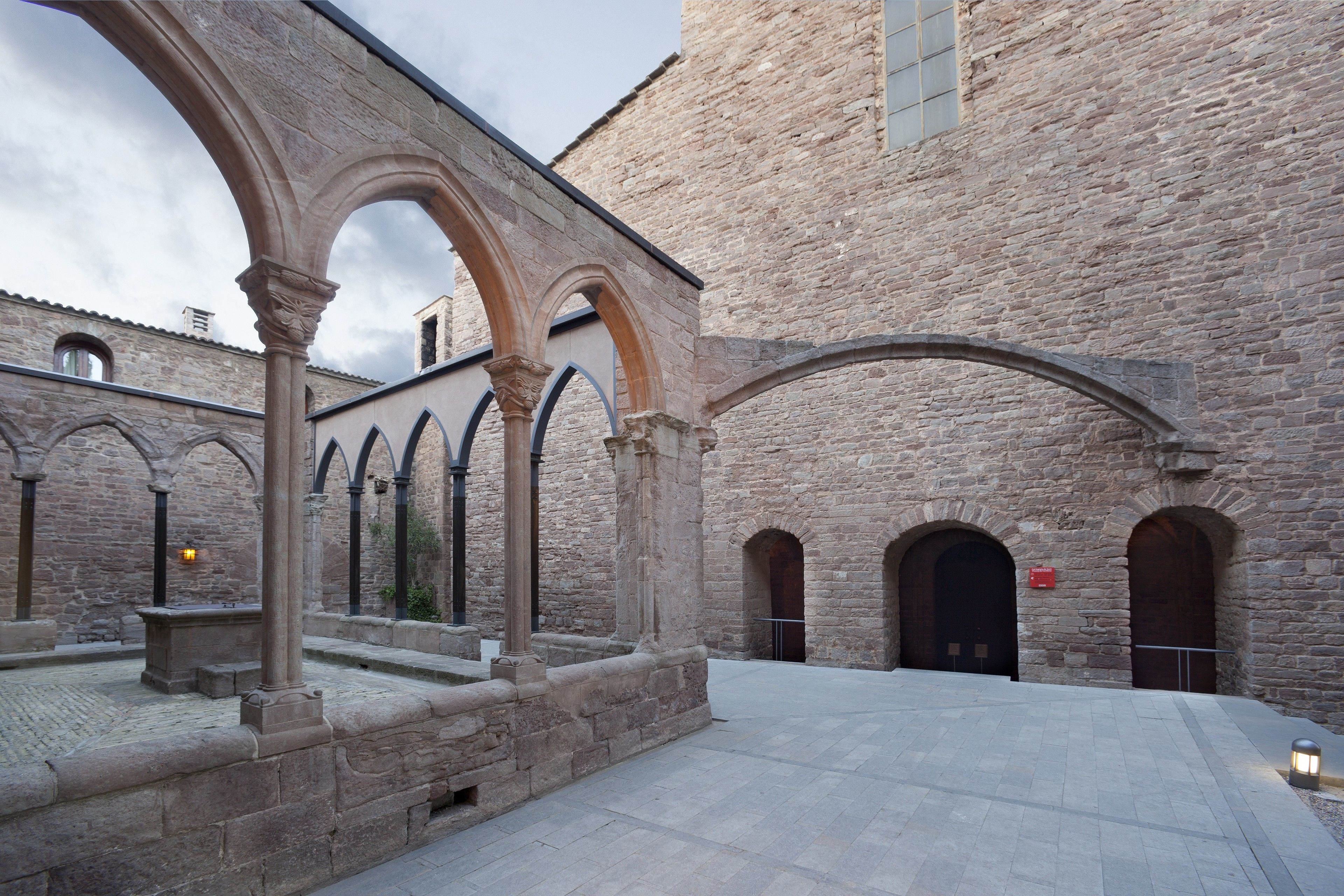 A courtyard with stone arches, a stone building, and a paved walkway.