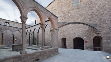 A courtyard with stone arches, a stone building, and a paved walkway.
