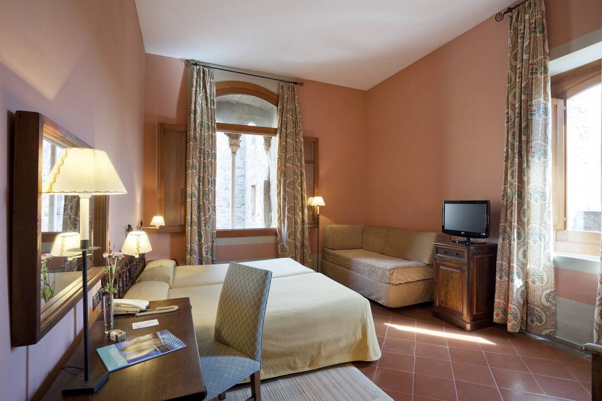Habitación de hotel con cama, escritorio con lámpara, televisión y sofá.