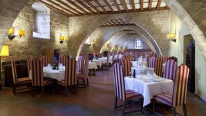 Un restaurante con paredes de piedra, vigas de madera y sillas a rayas. Las mesas están dispuestas con manteles blancos y copas de vino.