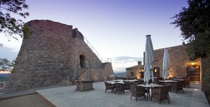 A stone building with a staircase leading up to a balcony. The balcony has tables and chairs, and there are umbrellas. - Parador de Cardona (Cardona)