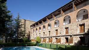Un patio con piscina, edificios de piedra y un cielo azul despejado.