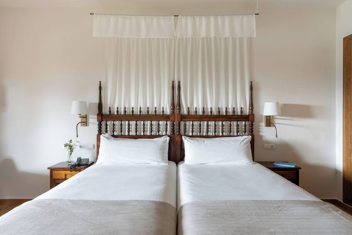 A double bed with a wooden headboard, two bedside tables with lamps, and a curtain above.