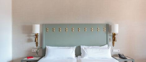 Una cama doble con sábanas blancas, dos mesitas de noche con lámparas y una lámpara de pared.