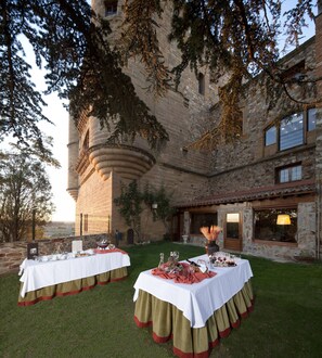 An outdoor dining setup with two tables, each with a white tablecloth and a red and green border, set against a stone building with a turret and ivy. - Parador De Benavente  (Benavente)