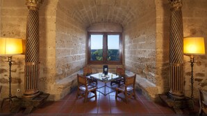 Un comedor con mesa y sillas, dos lámparas decorativas y vistas por una ventana.