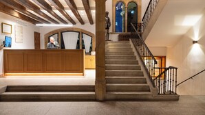 Un área de recepción con un escritorio de madera, una escalera con barandilla y una estatua.