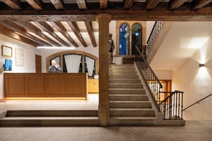 Un área de recepción con un escritorio de madera, una escalera con barandilla y una estatua.