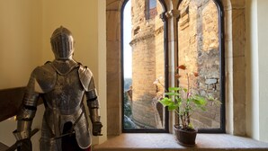 Una armadura de caballero en una habitación con ventana que da a un edificio de piedra.