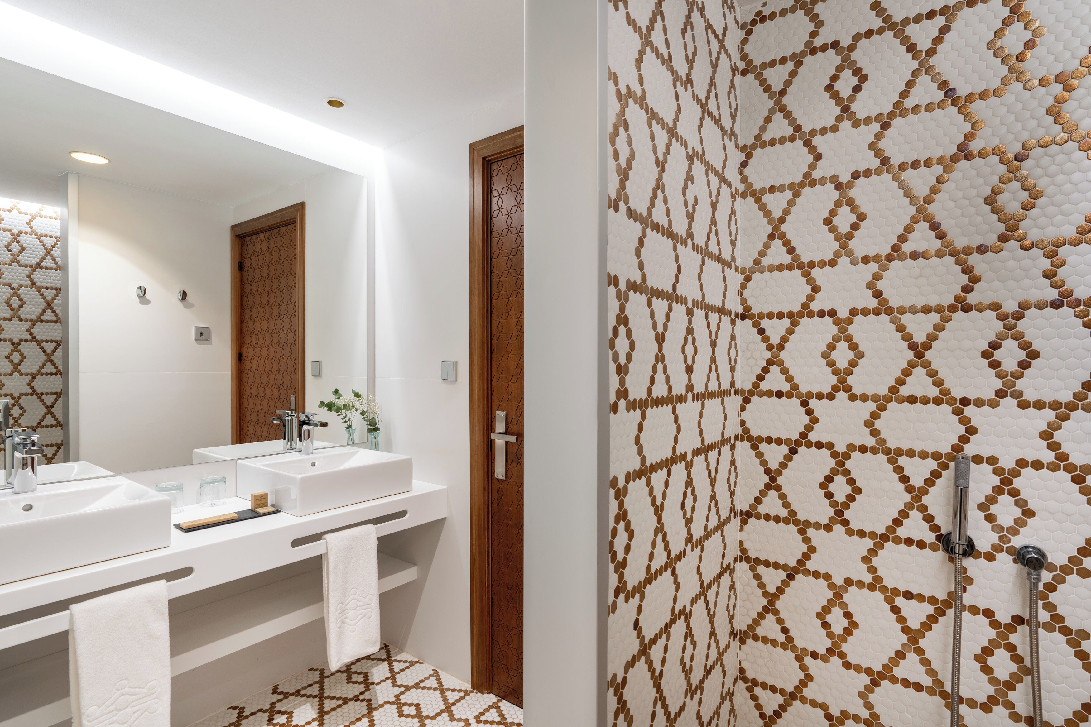 A modern bathroom with two sinks, a large mirror, and a shower with a patterned wall.