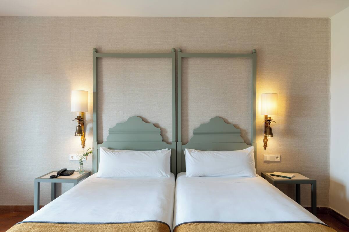 A double bed with a wooden headboard, two bedside tables with lamps, and a wall-mounted light fixture.