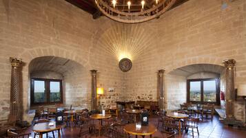 A historic interior with stone walls, wooden tables, and arched windows.