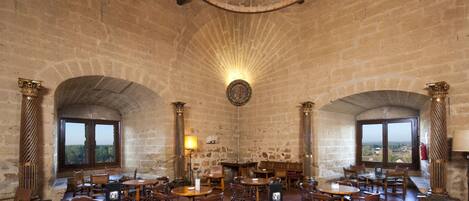 A historic interior with stone walls, wooden tables, and arched windows.