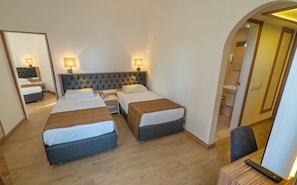 Ein Hotelzimmer mit zwei Betten, einem Nachttisch mit Lampe, einem Spiegel und einem durch einen Bogen sichtbaren Badezimmer.