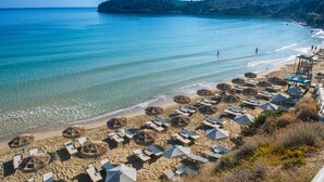 Una spiaggia con file di lettini e ombrelloni, un mare cristallino e un paesaggio collinare sullo sfondo.