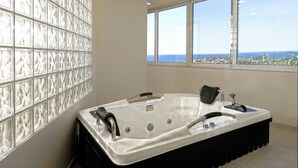 Un bagno moderno con una vasca da bagno ampia, un box doccia in vetro e vista sull'oceano attraverso ampie finestre.