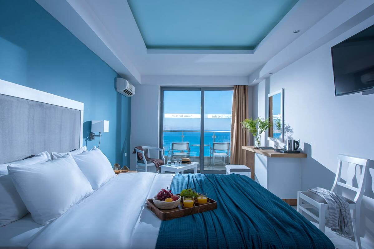 Ein modernes Hotelzimmer mit einem großen Bett, einem Frühstückswagen, einem Schreibtisch und Meerblick.