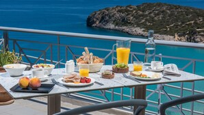 Una tavola imbandita per la colazione, con diversi cibi e bevande, affacciata su un panorama costiero mozzafiato.